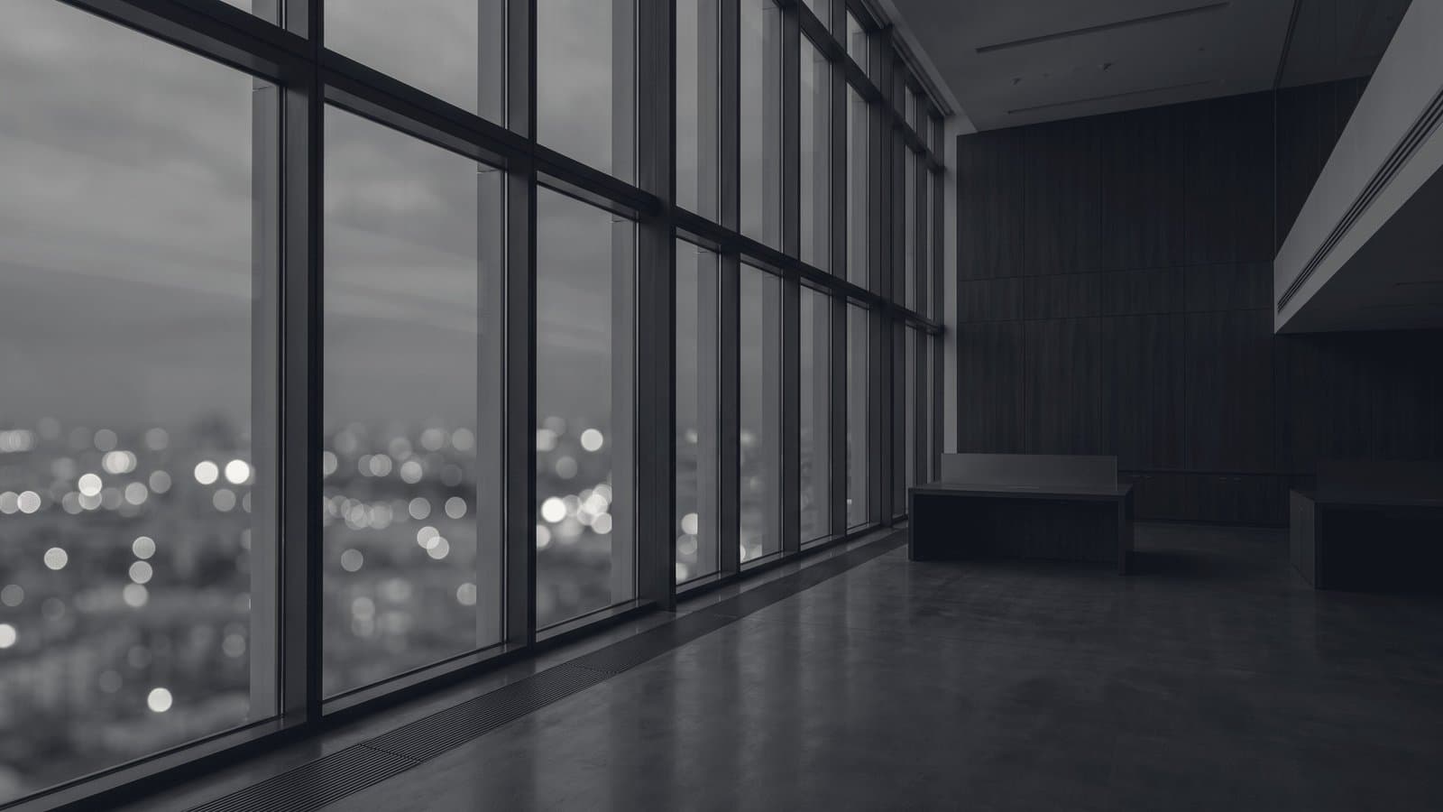 An empty high-floor office at dusk, city lights beyond the glass thrown out of focus.